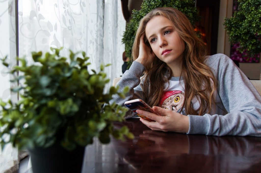 ung-kvinde-sidder-ved-et-bord-med-sin-mobiltelefon-og-keder-sig-kedsomhed